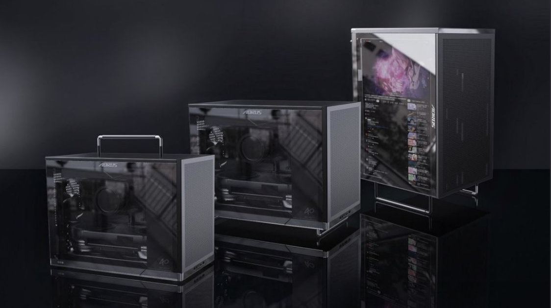 Trois boîtiers informatiques de tailles différentes, de la marque AORUS, sont alignés. Le plus grand dispose d'un écran numérique affichant une interface YouTube.