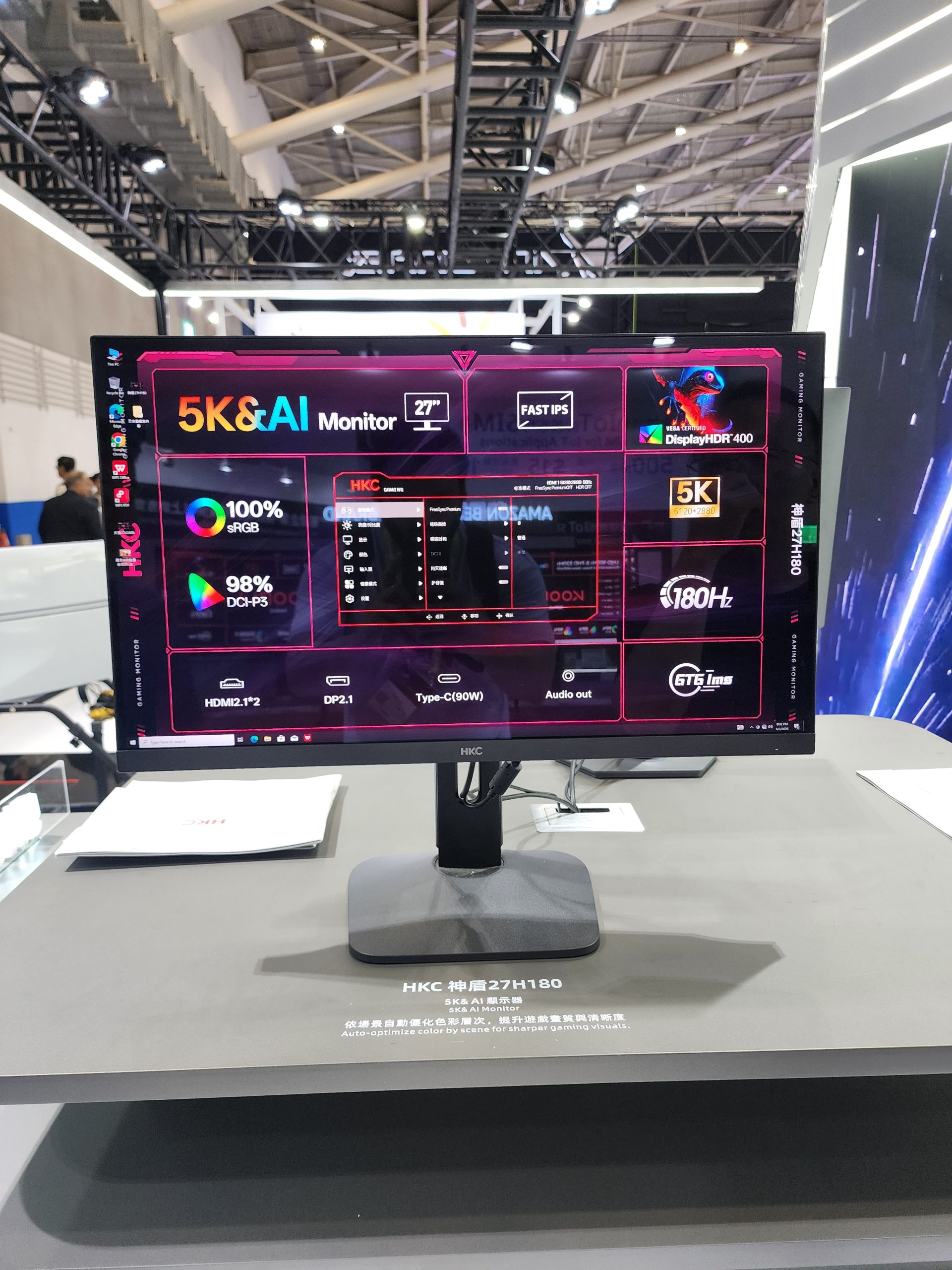 Le moniteur HKC 27H180 5K affiche des spécifications comme '5K&AI Monitor', 'Fast IPS', '27 DisplayHDR 400' et '180Hz' sur un stand d'exposition.