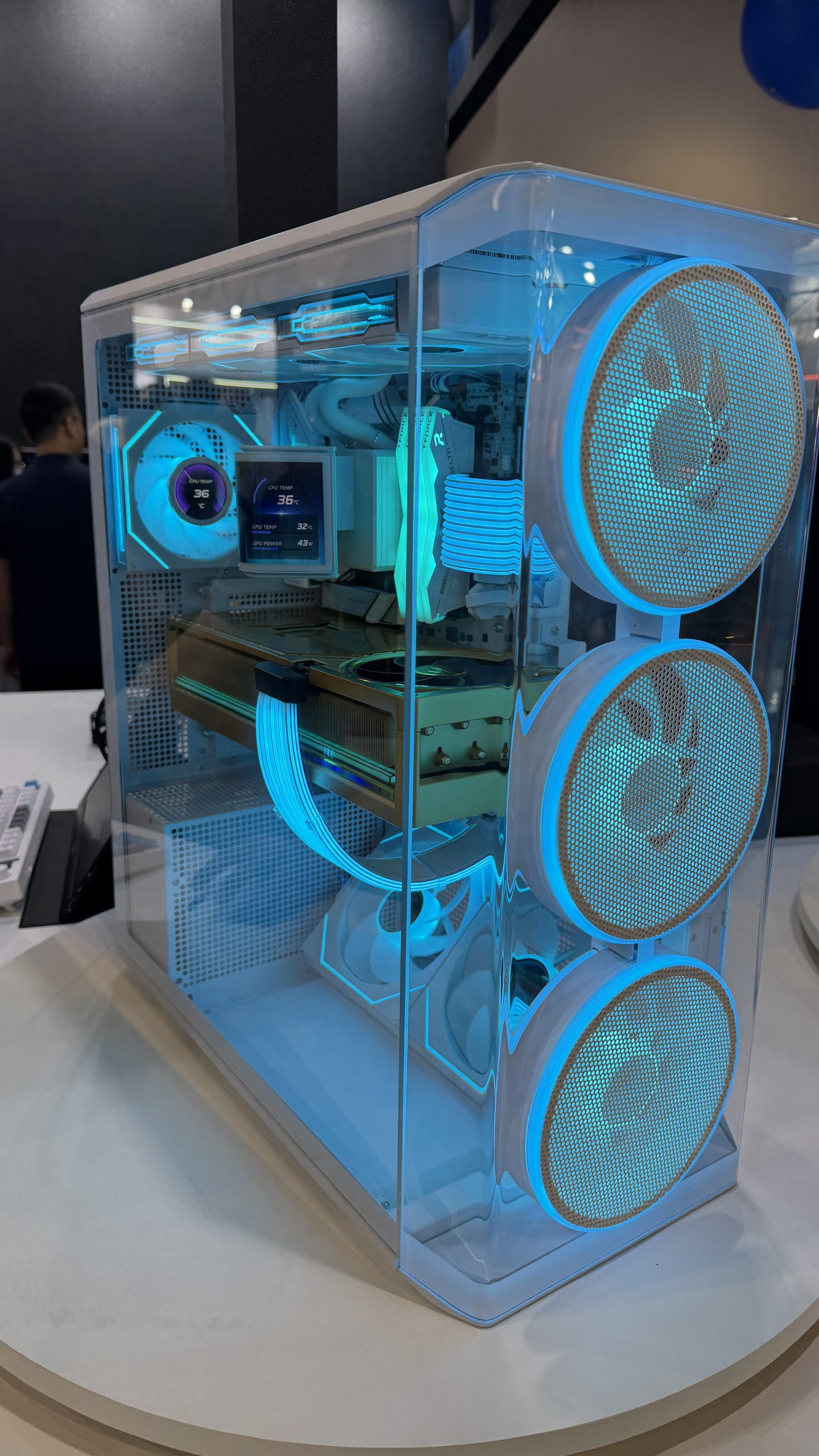 Boîtier PC avec éclairage LED bleu, trois ventilateurs avant, un GPU visible, câbles tressés et affichage digital montrant les températures CPU et GPU.