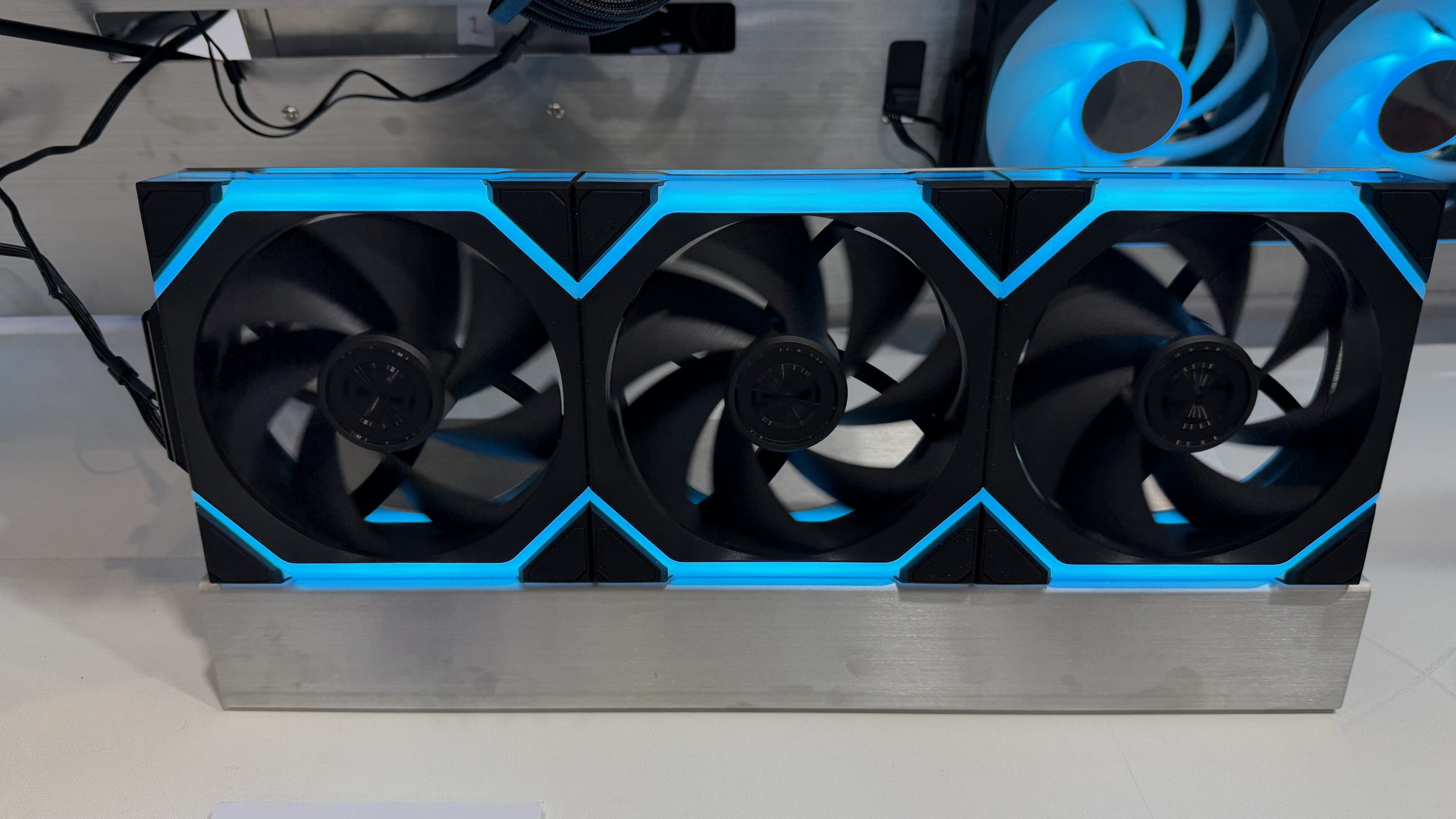 Trois ventilateurs de refroidissement non marqués avec un éclairage LED bleu montés sur un support métallique.