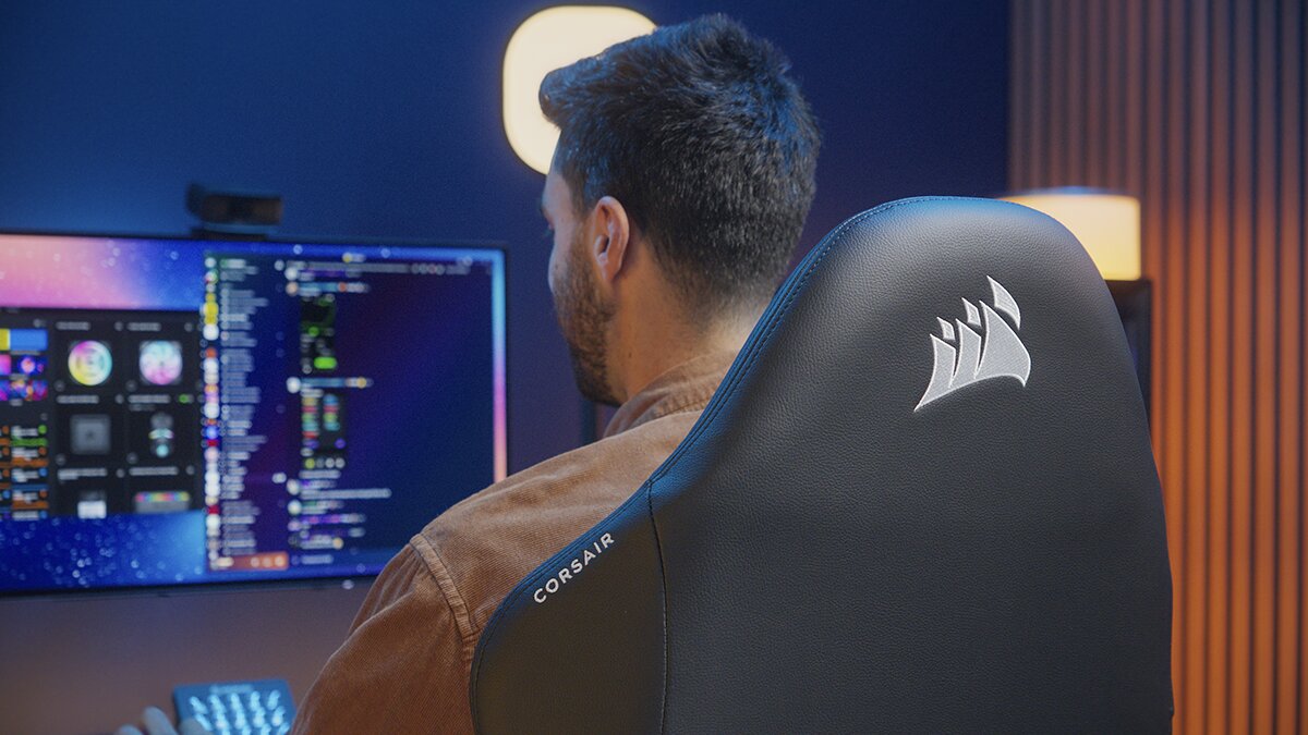 Une personne assise à un bureau utilisant un ordinateur, le dossier d'un siège gaming Corsair visible au premier plan.