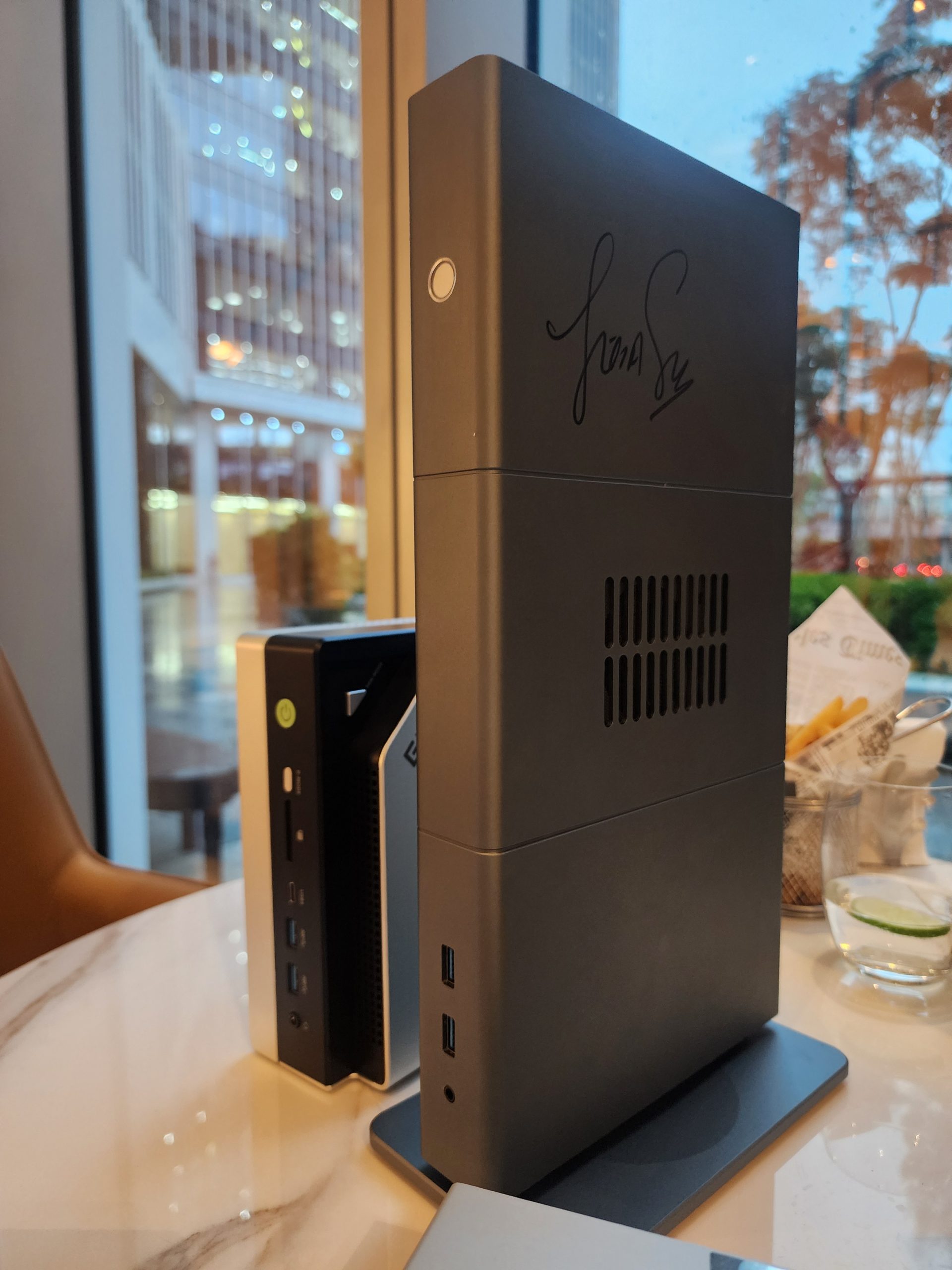 Trois mini PC alignés sur une table en marbre, dont le plus grand est signé. Les deux plus petits modèles montrent leurs ports USB avant.