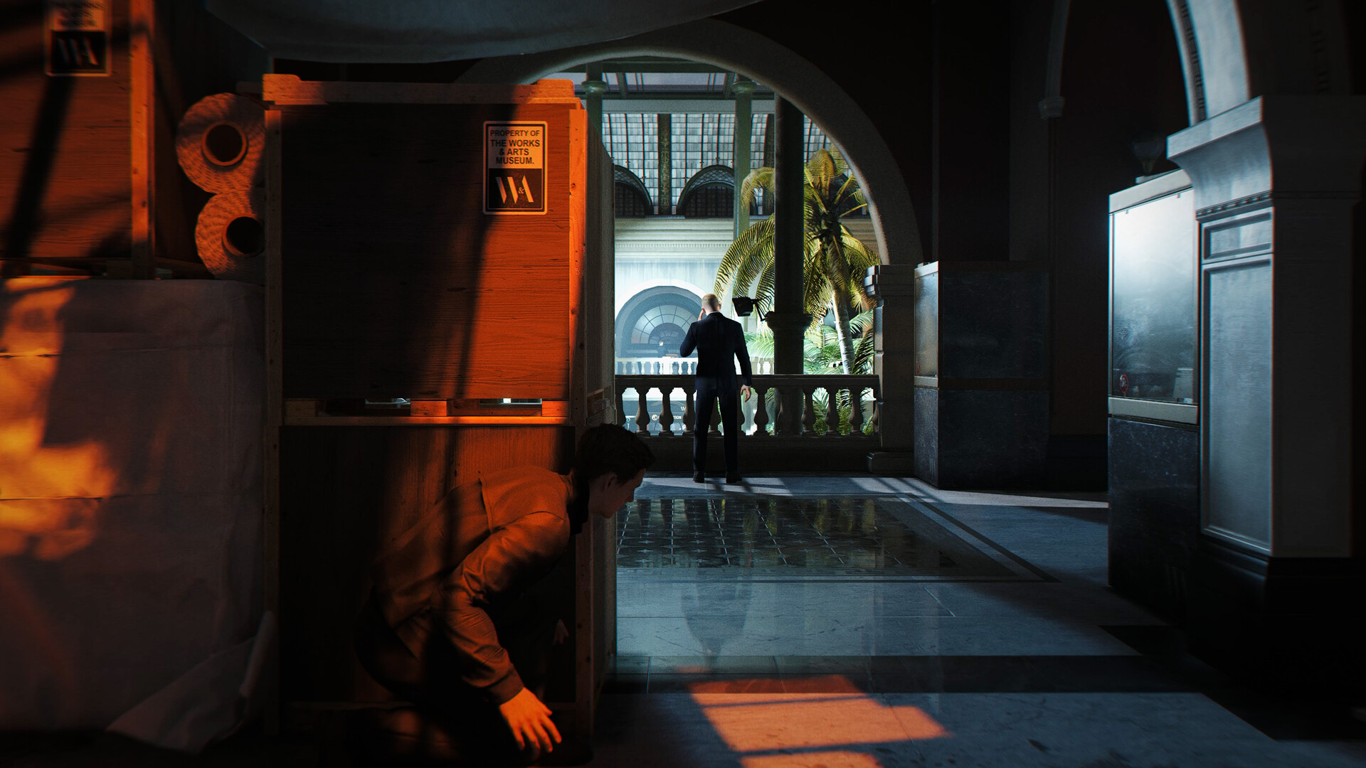 Un personnage de 'Hitman' accroupi derrière une caisse dans un décor de musée.