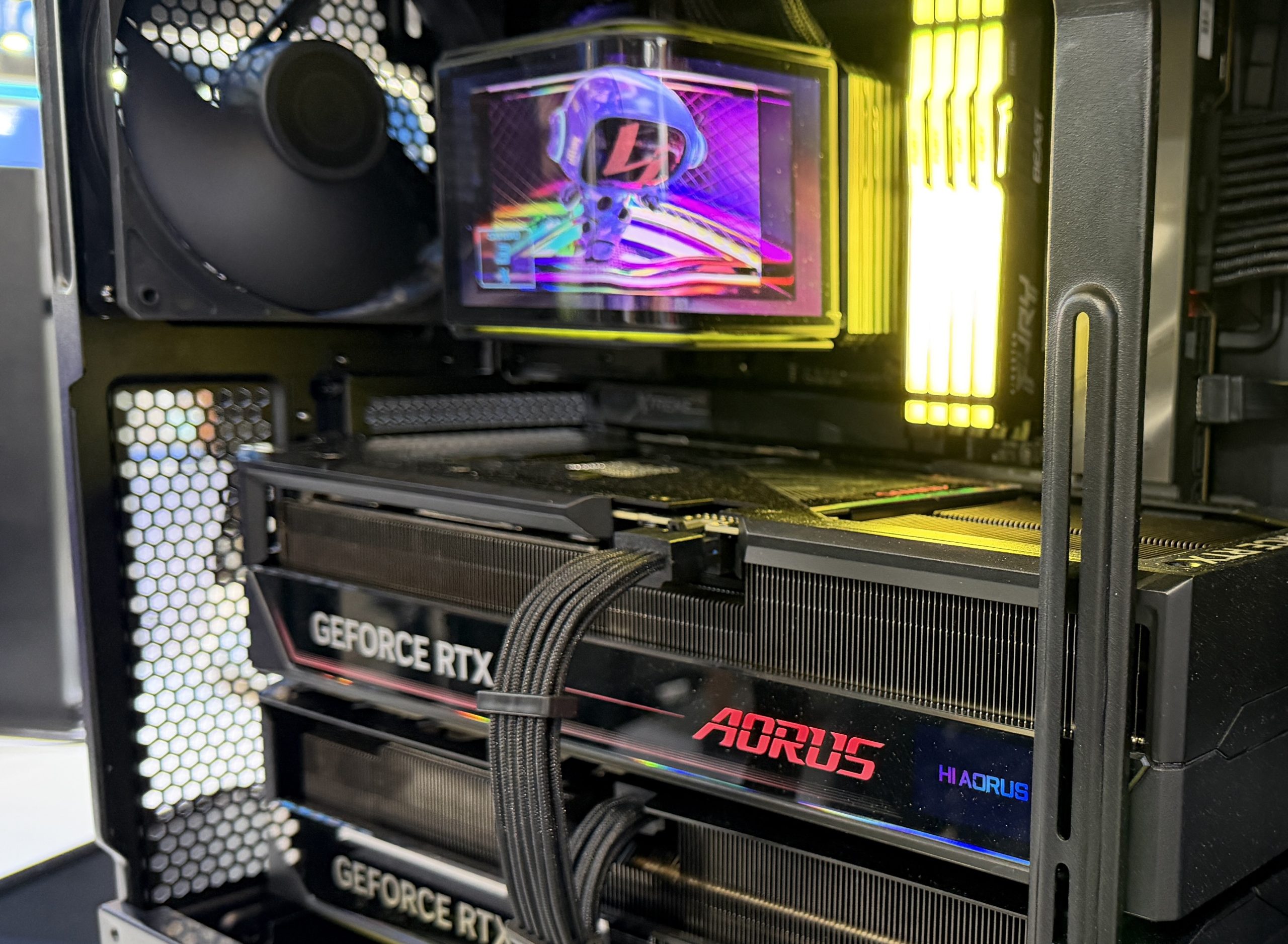 Une tour ouverte exposant deux cartes graphiques GeForce RTX, un refroidissement à eau AORUS avec affichage et des barrettes de RAM illuminées.