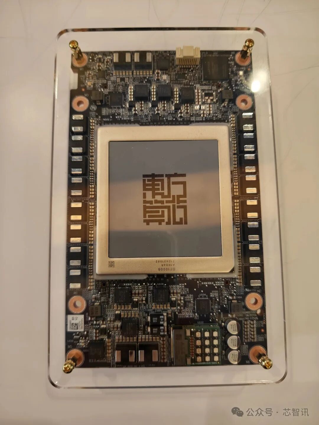Une carte de circuit avec une grande puce centrale au design rappelant un QR code, entourée de composants plus petits.