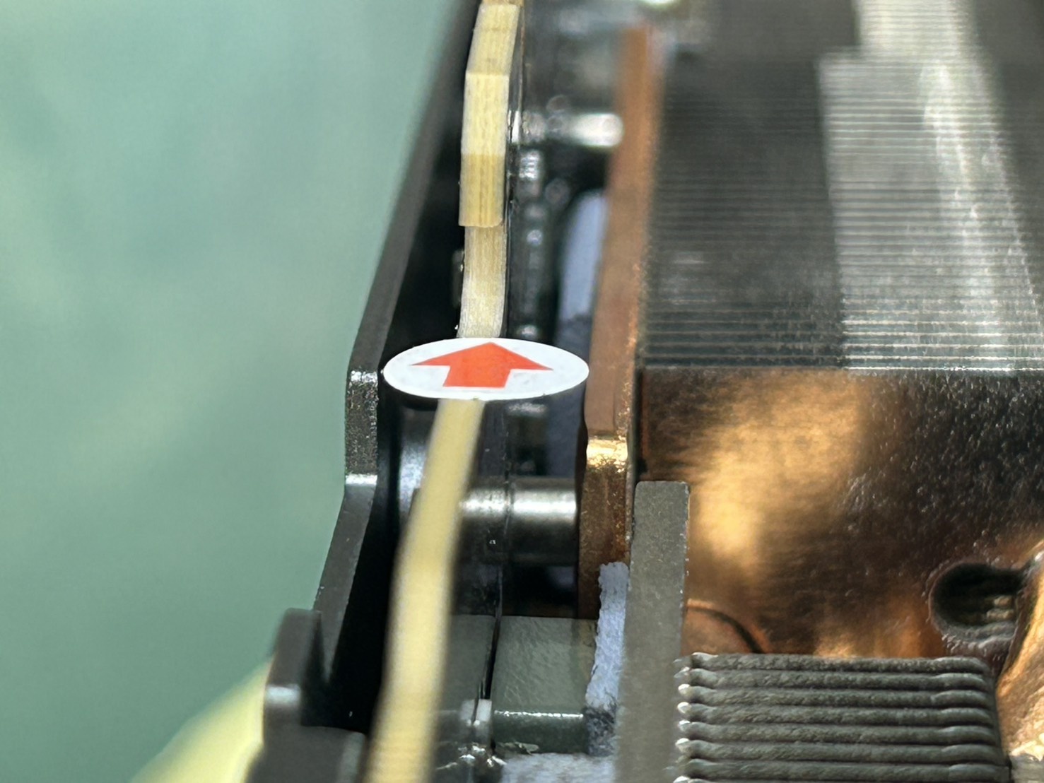 Gros plan sur le dissipateur d’un GPU avec un autocollant blanc et une flèche rouge indiquant le sens du flux d’air.