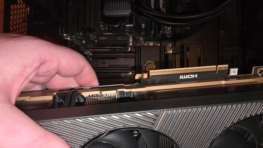 Une main installe une carte graphique NVIDIA GeForce dans un boîtier d'ordinateur, avec des barrettes de RAM Crucial visibles.