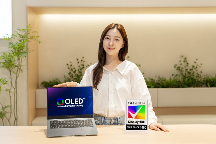 Une personne présente un portable Samsung affichant 'OLED verified by Samsung Display', à côté d'une signalétique pour 'VESA Certified DisplayHDR True Black 1400'.