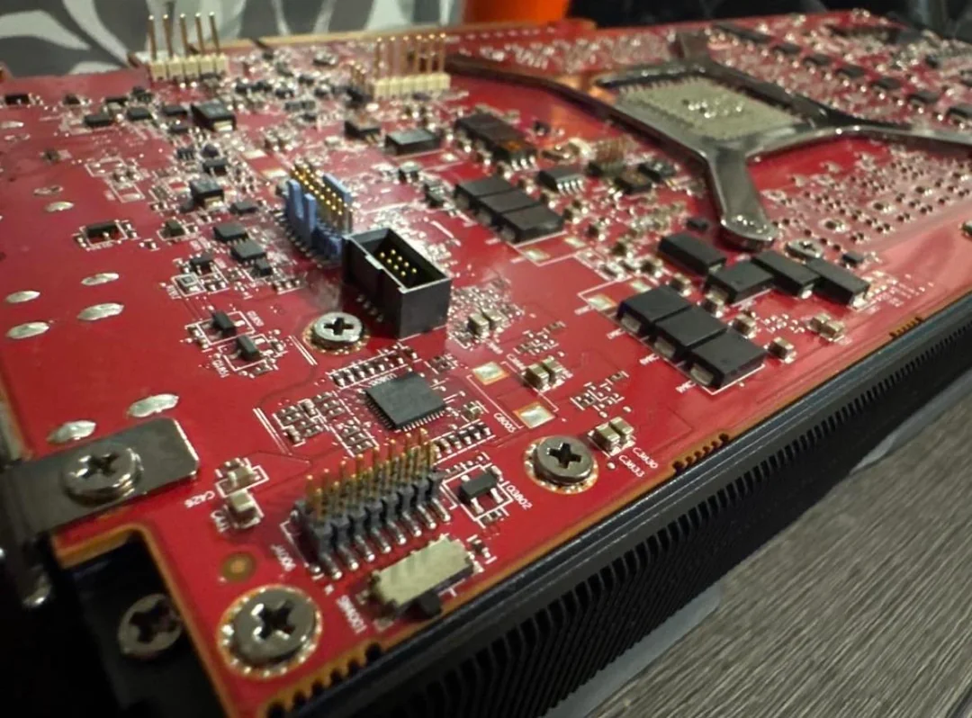 Détail de l'arrière d'un GPU avec un circuit imprimé rouge, montrant divers composants électroniques et connecteurs.