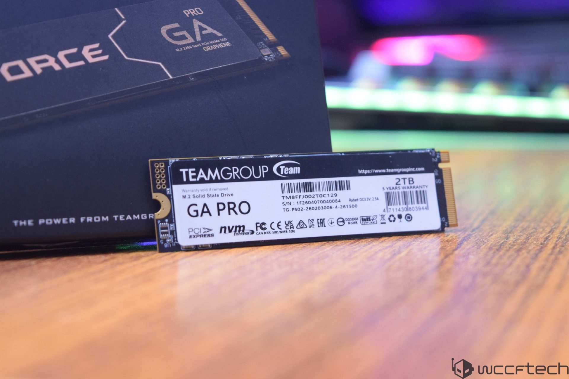 Un SSD Teamgroup T-Force GA Pro NVMe 2 To est affiché sur une surface en bois avec son emballage en arrière-plan.