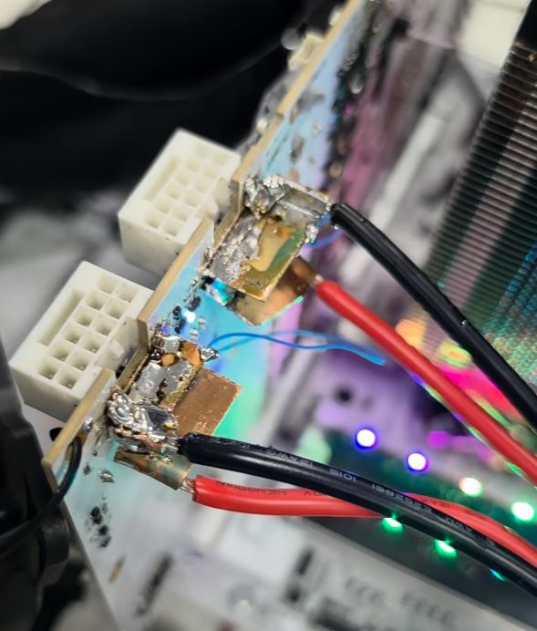 Gros plan sur une carte électronique personnalisée avec des connecteurs d'alimentation soudés et des fils, dans un setup PC éclairé par des RGB.