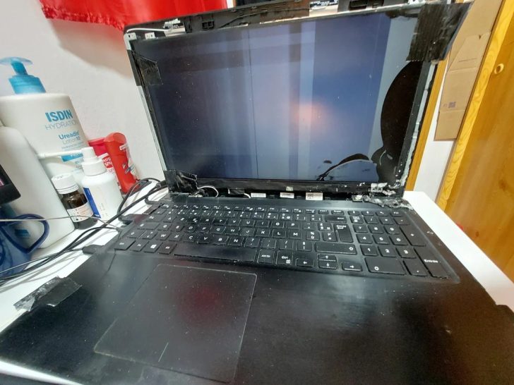 Un portable endommagé avec l'écran brisé est posé sur un bureau à côté de produits de soin.