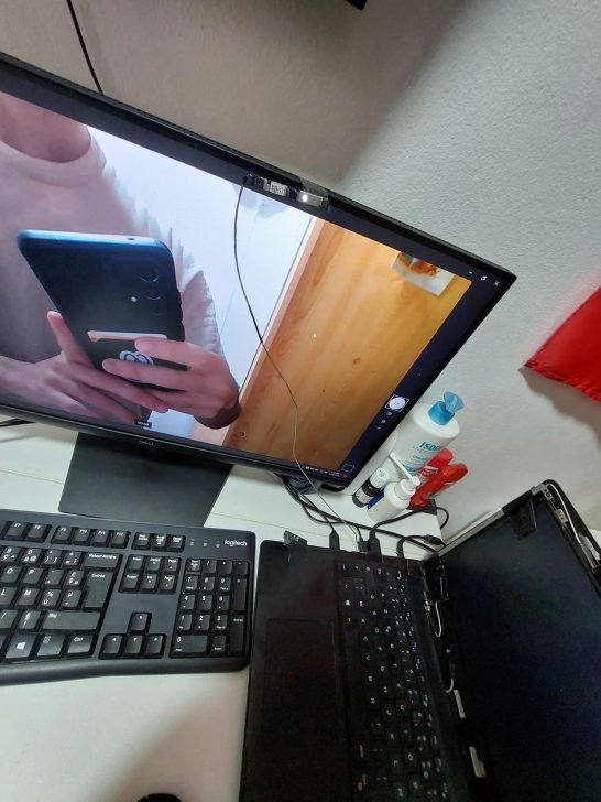 Un moniteur Dell avec un clavier Logitech et un portable entrouvert, une webcam est fixée au moniteur.