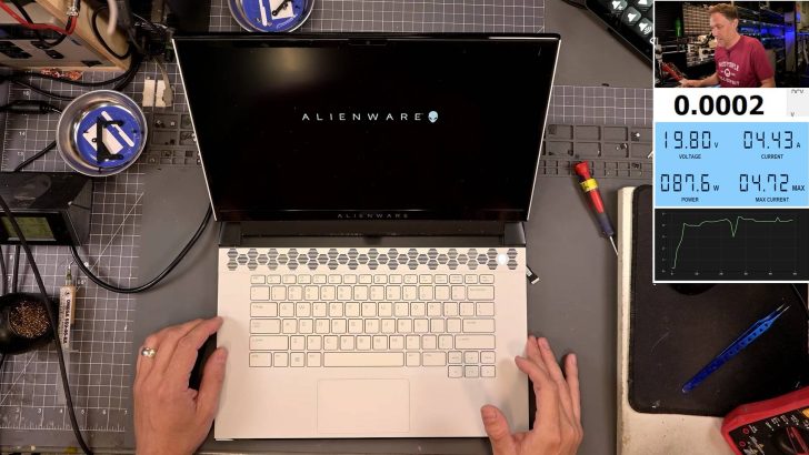 A top view of an Alienware laptop on a workbench, with a screen displaying 'ALIENWARE,' alongside a monitor showing power and current readings: '19.80V,' '4.43A,' '087.6W.'