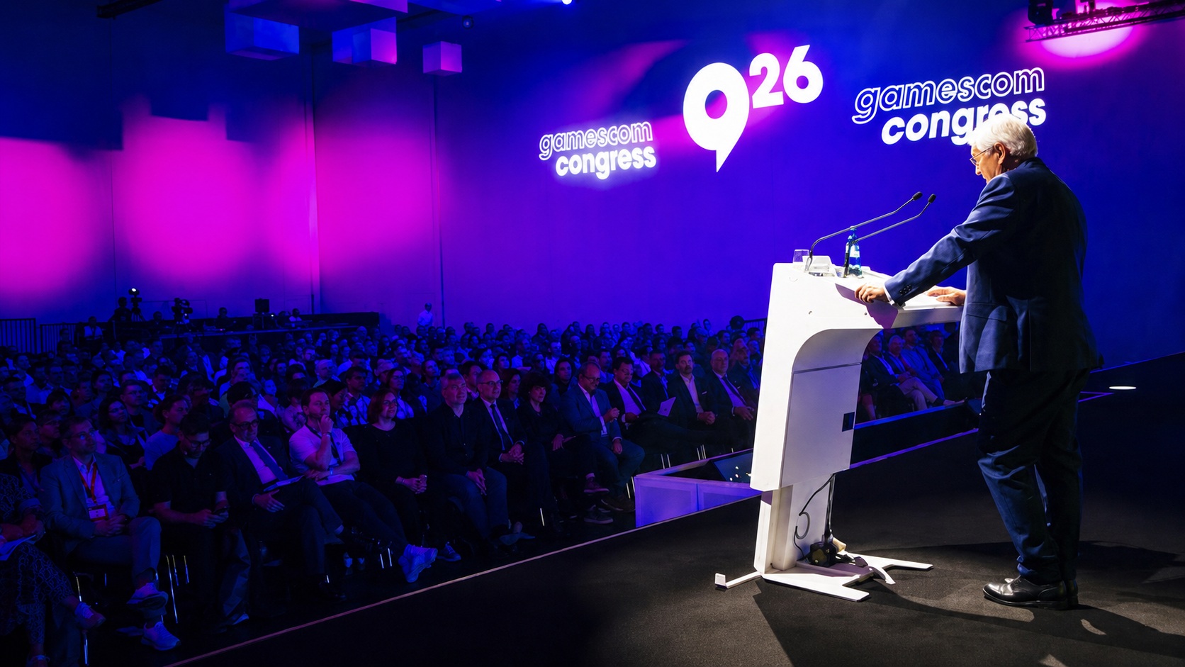Un intervenant s'adresse au public du 'gamescom congress 2026' sous un éclairage violet.