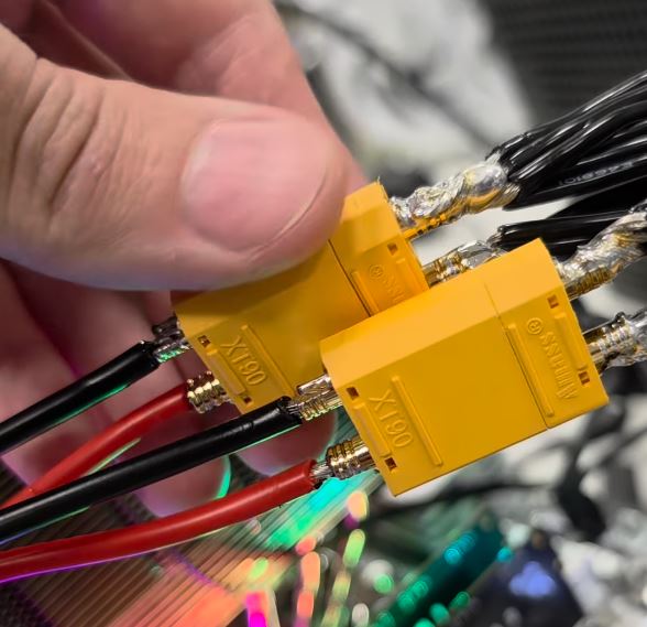 Une main tenant des connecteurs Amass XT90 jaunes avec des fils rouges et noirs attachés.
