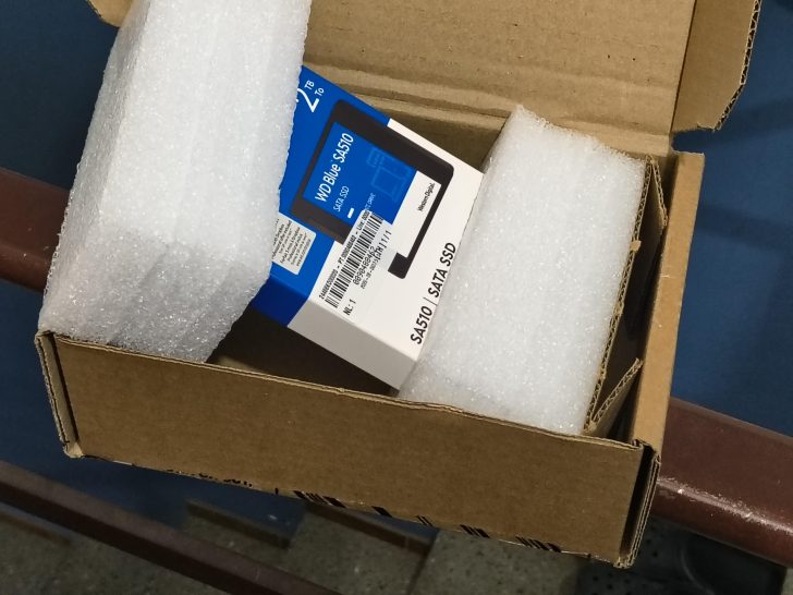 Un SSD SATA Western Digital WD Blue SA510 1TB partiellement déballé dans une boîte carton avec mousse de protection.