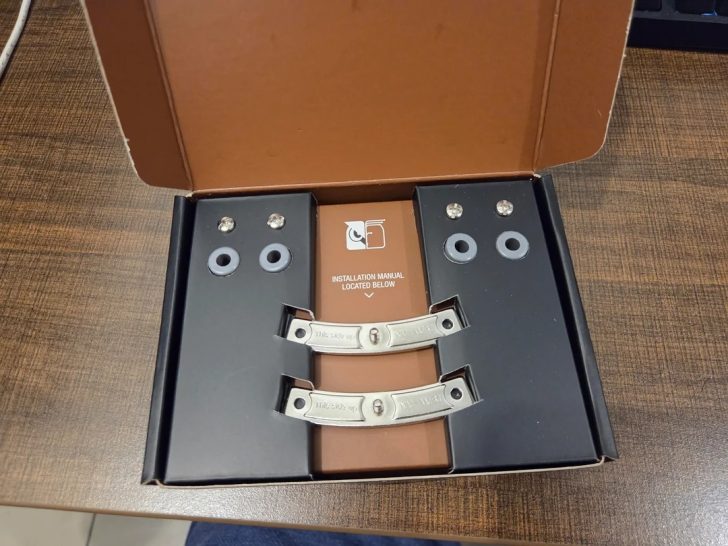 Un kit de montage Noctua SecuFirm à l'intérieur d'une boîte posée sur une table en bois, avec un manuel d'installation visible.