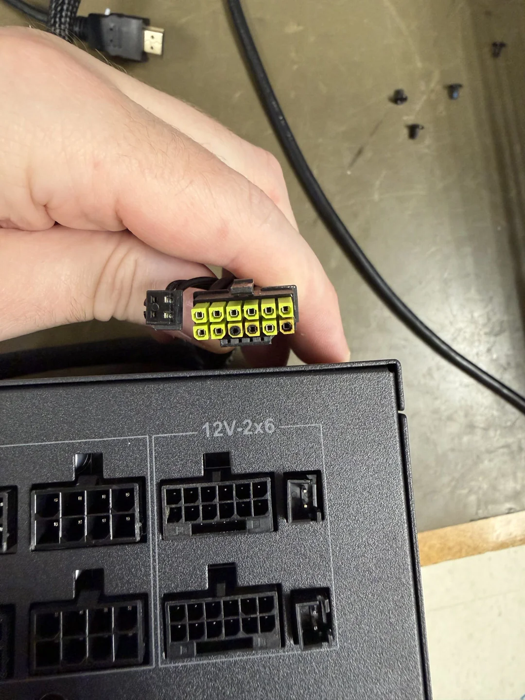 Une main tenant un connecteur d'alimentation 12V 2x6 au-dessus d'une alimentation.