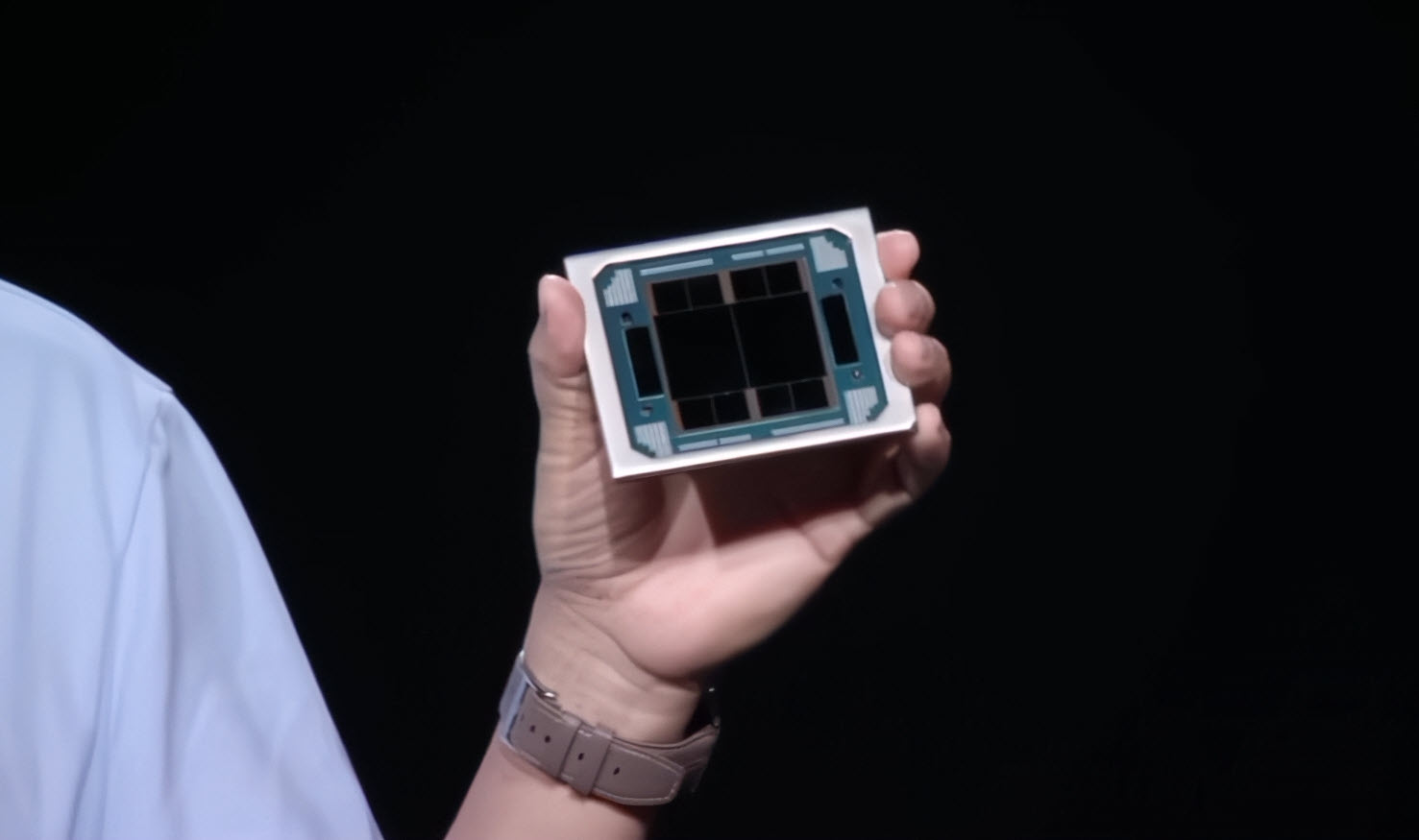 Une personne tenant une puce AMD MI300, dont les composants et les détails de conception sont visibles, sur fond sombre.