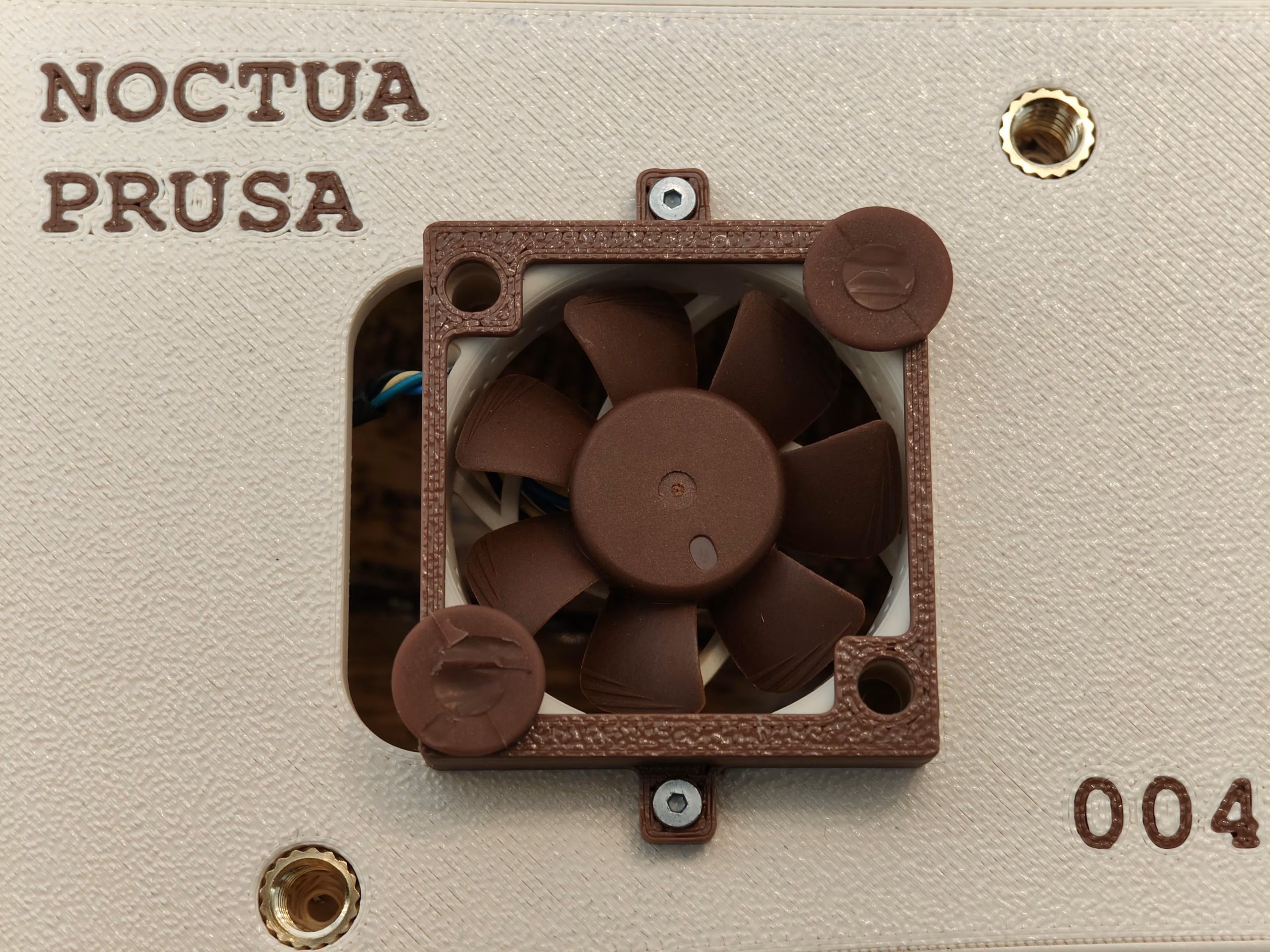 A Noctua cooling fan is mounted on a beige Prusa 3D printer panel, with the text 'NOCTUA PRUSA' and a serial number '004'.