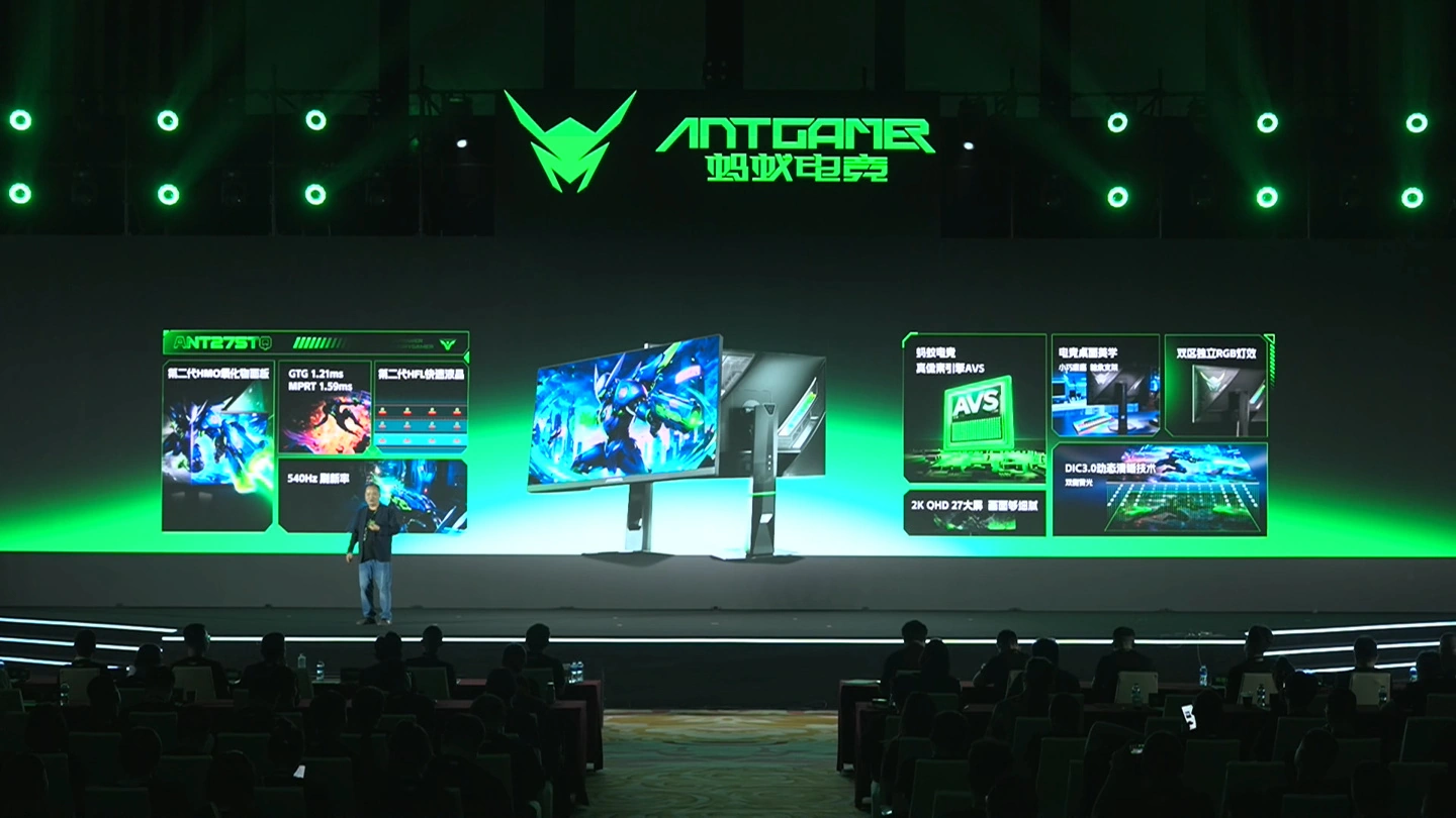 A presenter on stage at an Antgamer event showcases monitors with features including 'GTG 1.2ms,' '540Hz refresh rate,' and '2K QHD 27-inch' displays.