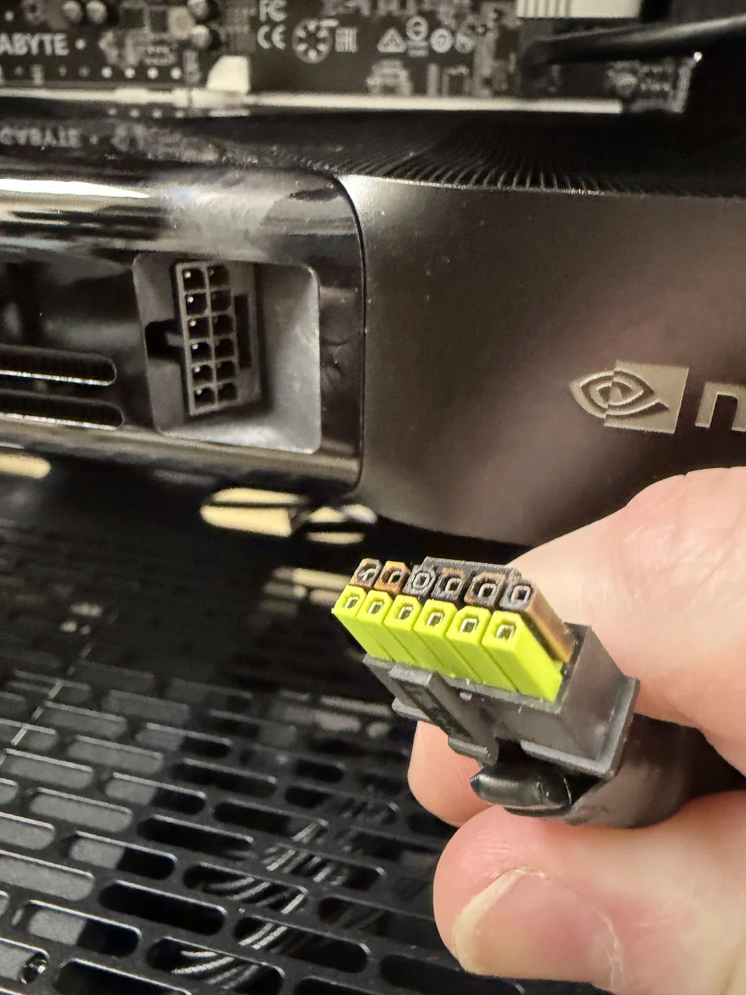 Gros plan d'une main tenant un connecteur 12VHPWR jaune et noir près d'une carte graphique NVIDIA.
