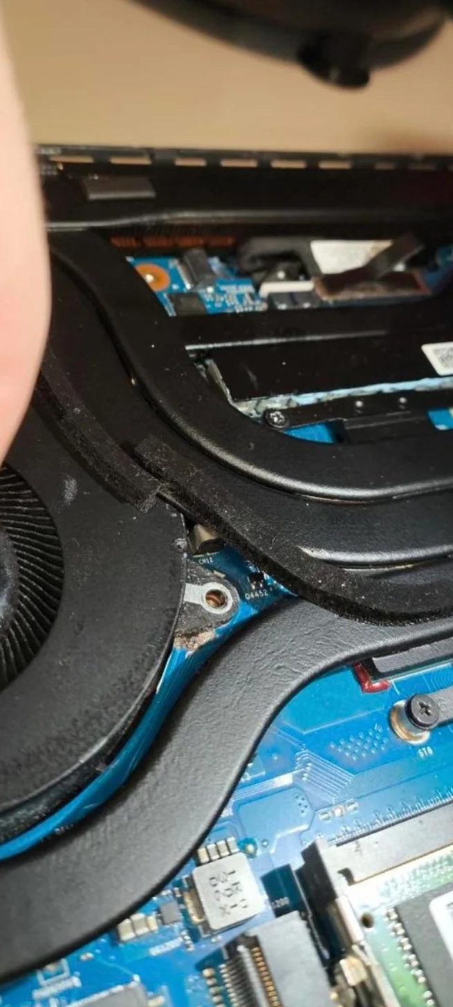 Vue rapprochée du système de refroidissement interne d'un ordinateur portable montrant deux caloducs, un ventilateur et une partie de la carte mère bleue.