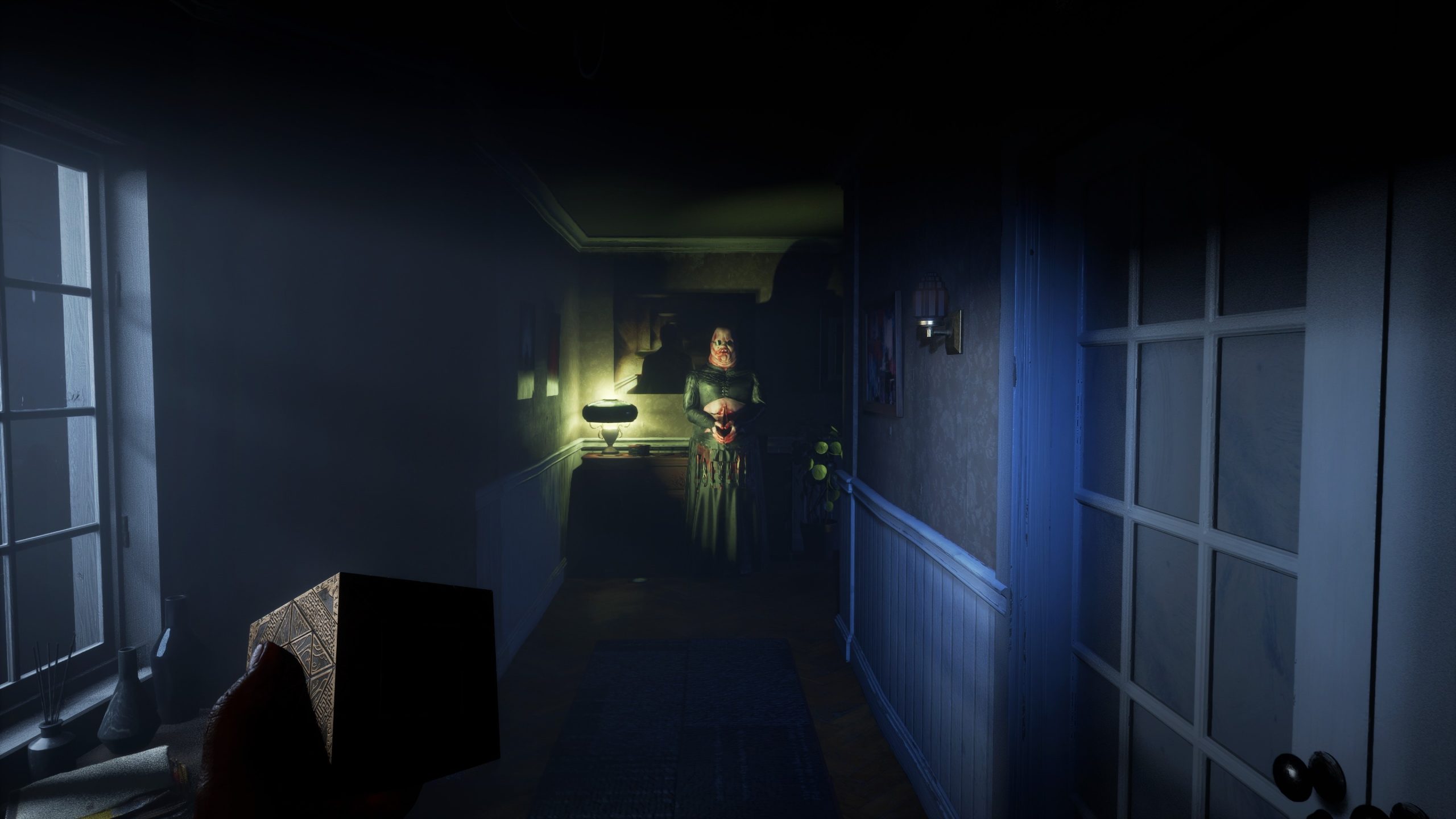 Un personnage dans un couloir sombre, tenant une lampe, avec une main tenant une boîte ornée au premier plan.