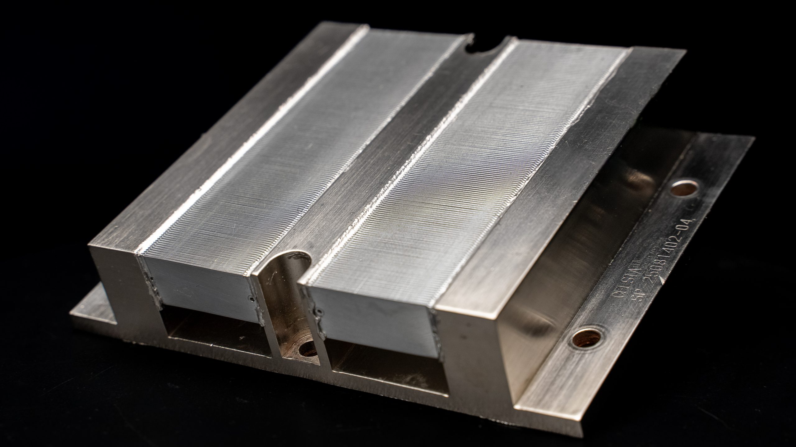 Vue rapprochée d’un dissipateur thermique métallique non marqué avec des ailettes rainurées et une gravure visible sur le côté.