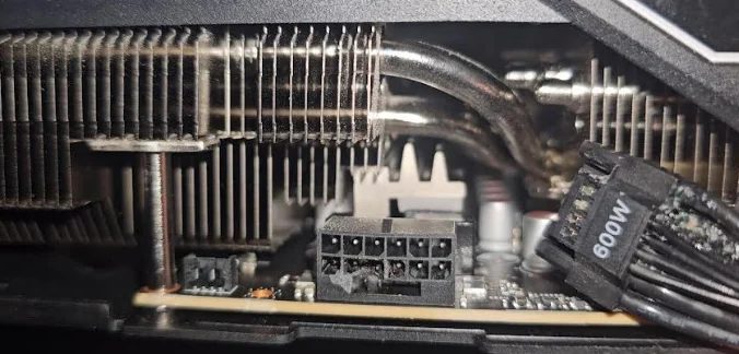 A close-up of a graphics card showing an uncovered 12-pin power connector and a power cable labeled '600W' beside the heat sink.
