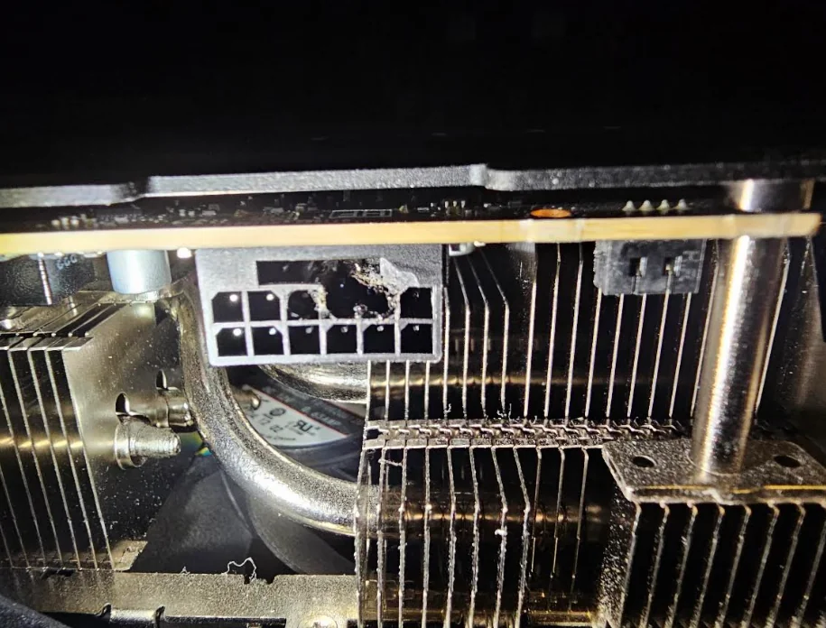 A damaged power connector is visible on a graphics card with metal heat sink fins surrounding it.