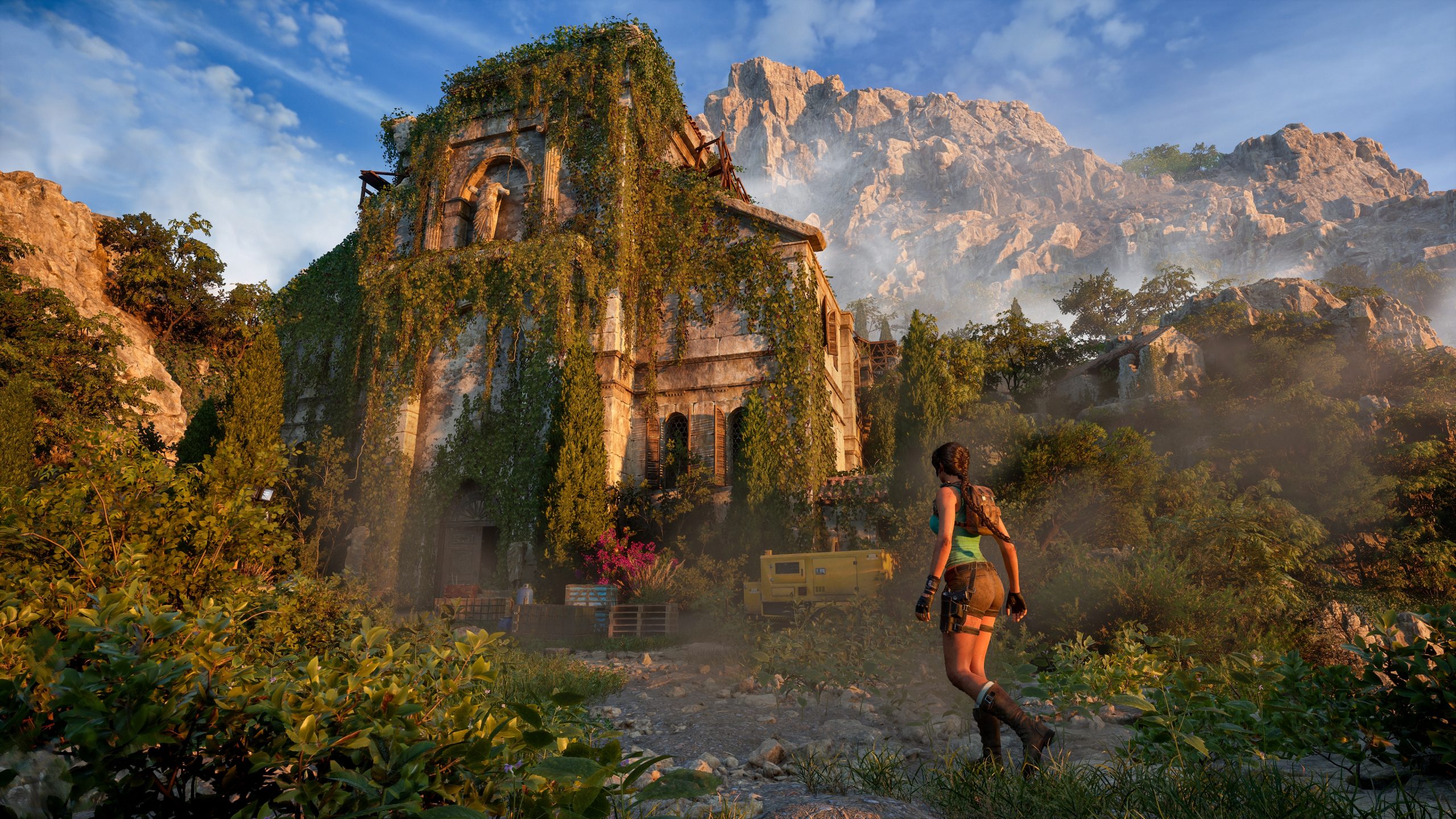 Lara Croft s'approche d'un bâtiment antique envahi par la végétation, devant un décor montagneux.