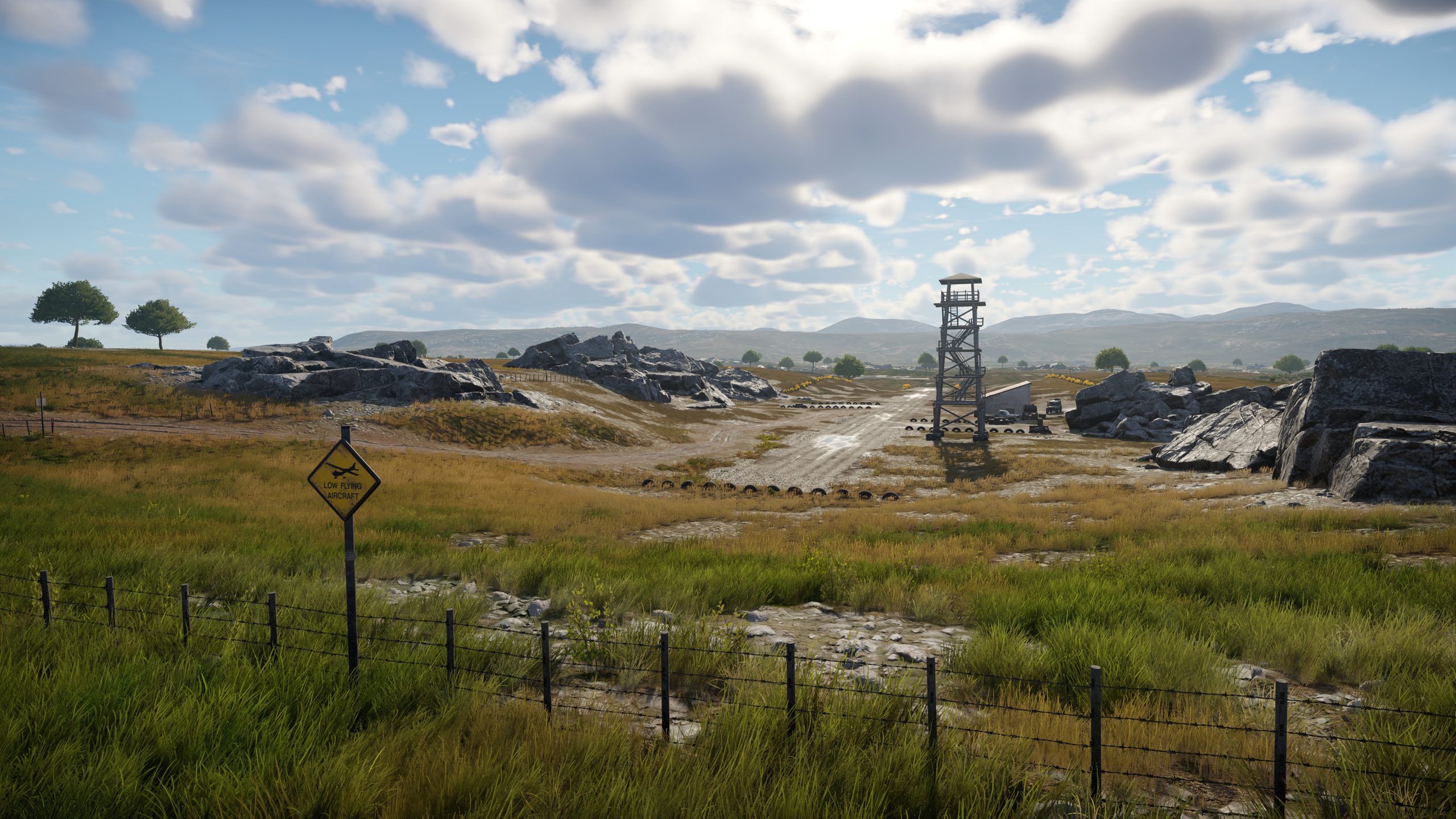 Une scène du jeu vidéo War Thunder représentant un paysage rural avec un chemin de terre, un poste de garde, des rochers et un panneau indiquant 'Low Flying Aircraft'.