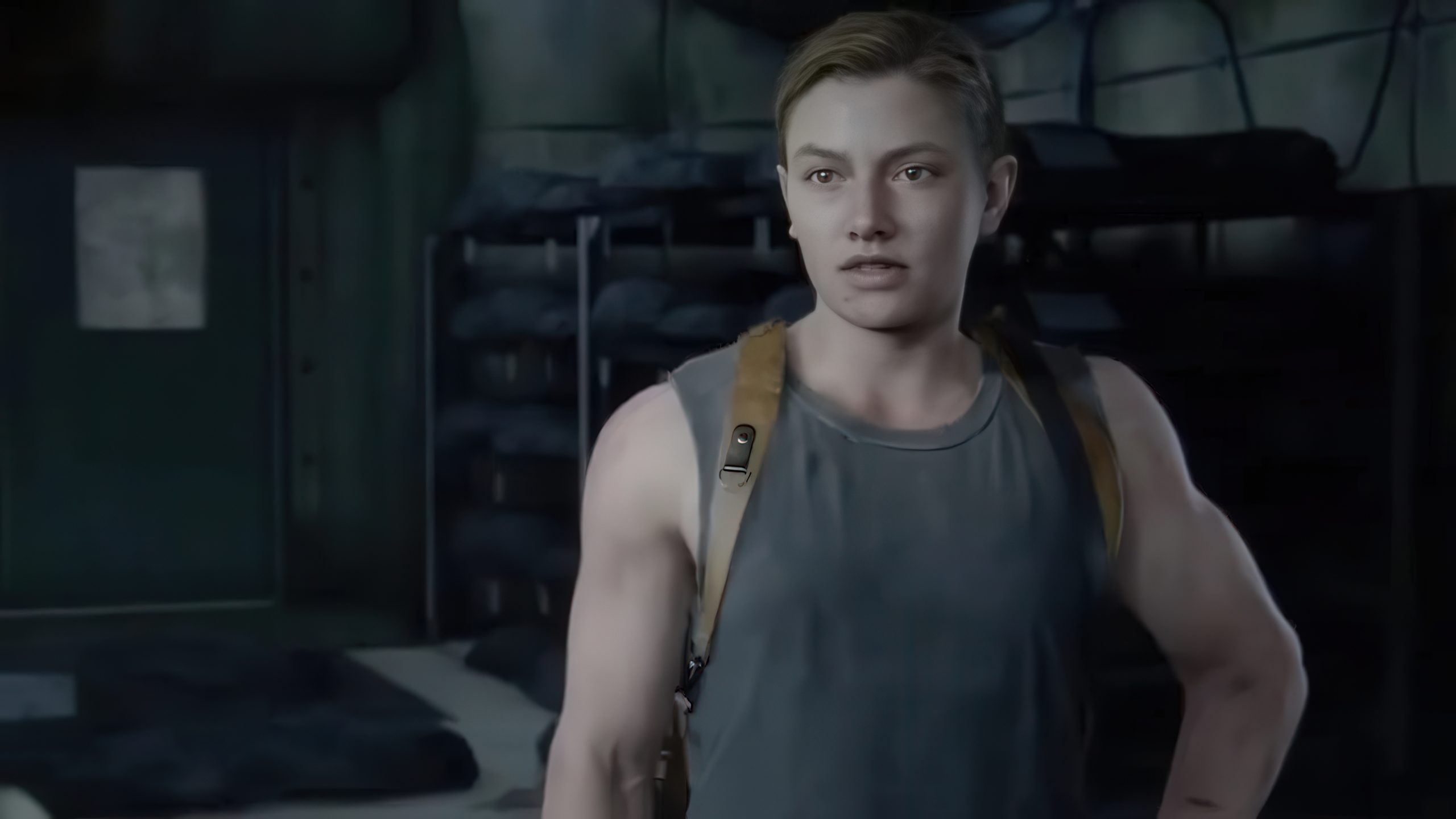 Abby, du jeu The Last of Us Part II, se tient dans une pièce faiblement éclairée, vêtue d'un débardeur avec les bretelles d'un sac à dos.
