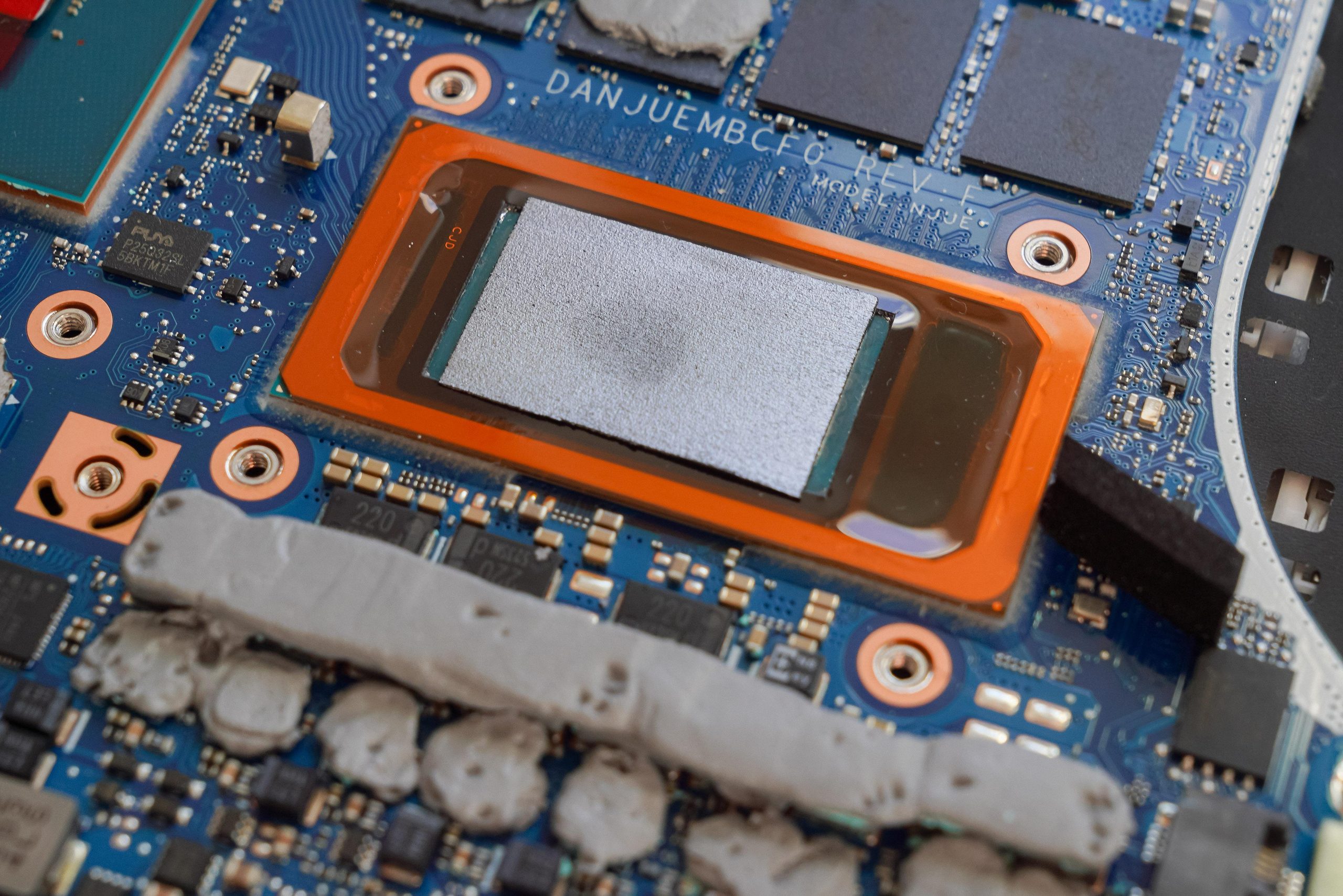A close-up of a laptop motherboard featuring a processor with visible thermal paste and text labeling, including 'DANJUEMBCF0' and 'REV 1.4'.