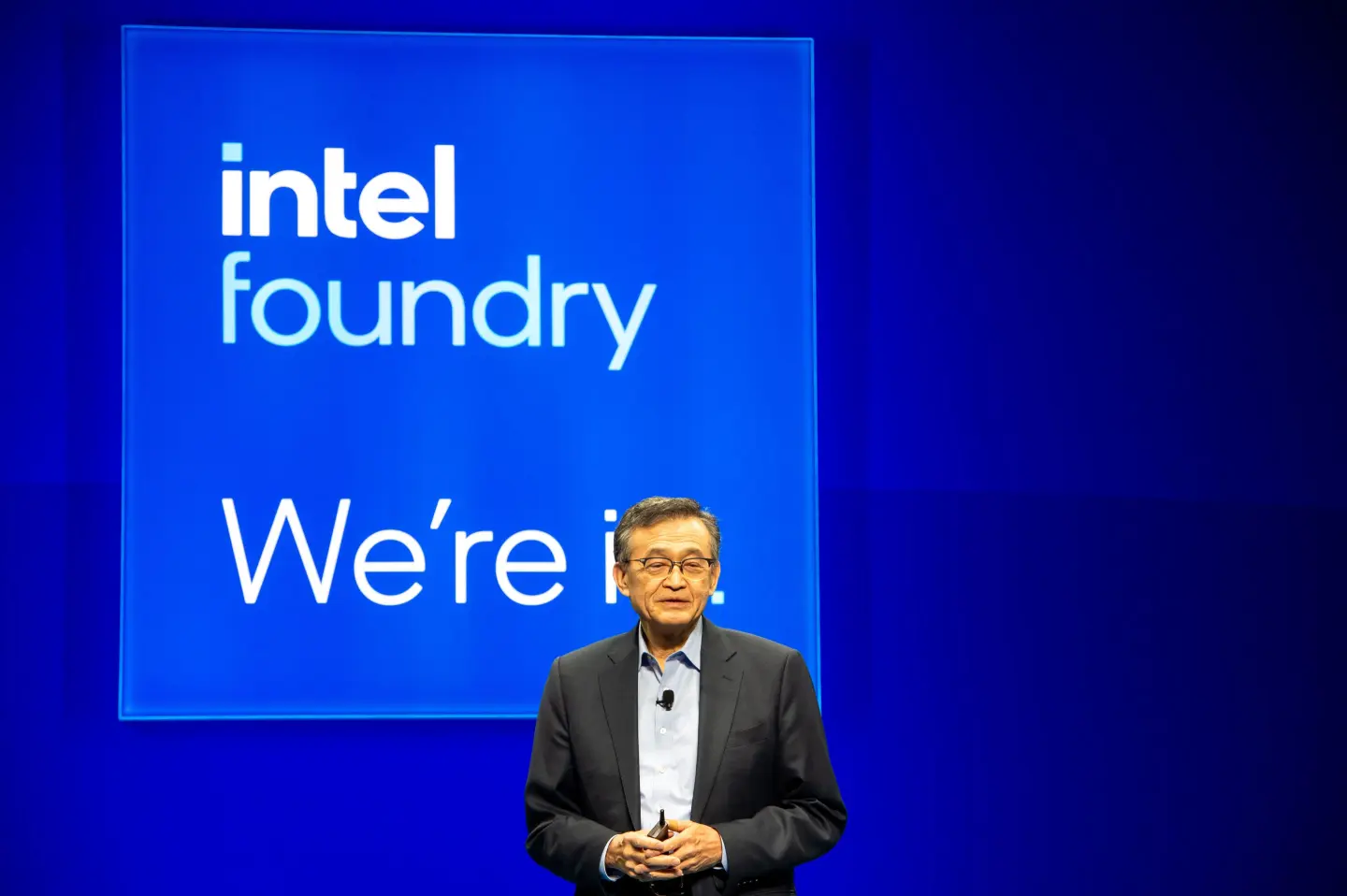 Un dirigeant se tient devant un écran bleu affichant 'intel foundry We're in.'
