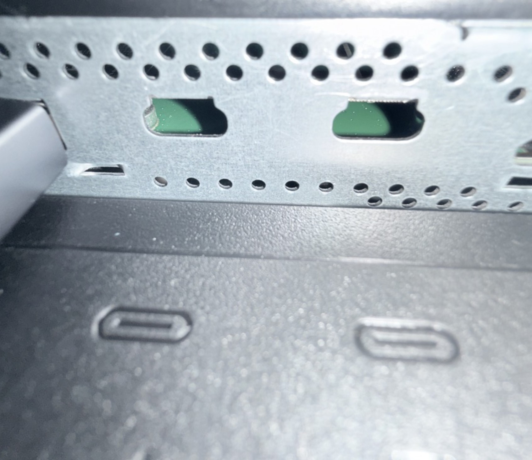 A close-up of a metal panel with ventilation holes and visible USB-C port markings on a piece of hardware.