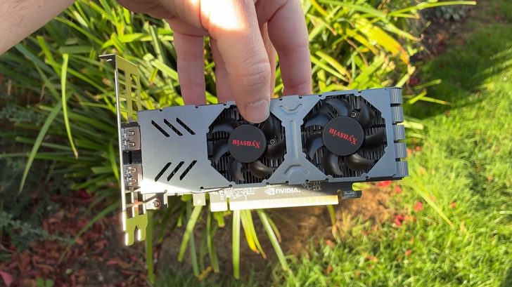 Une personne tient une carte graphique Masuax à deux ventilateurs, avec le logo NVIDIA visible, en extérieur.