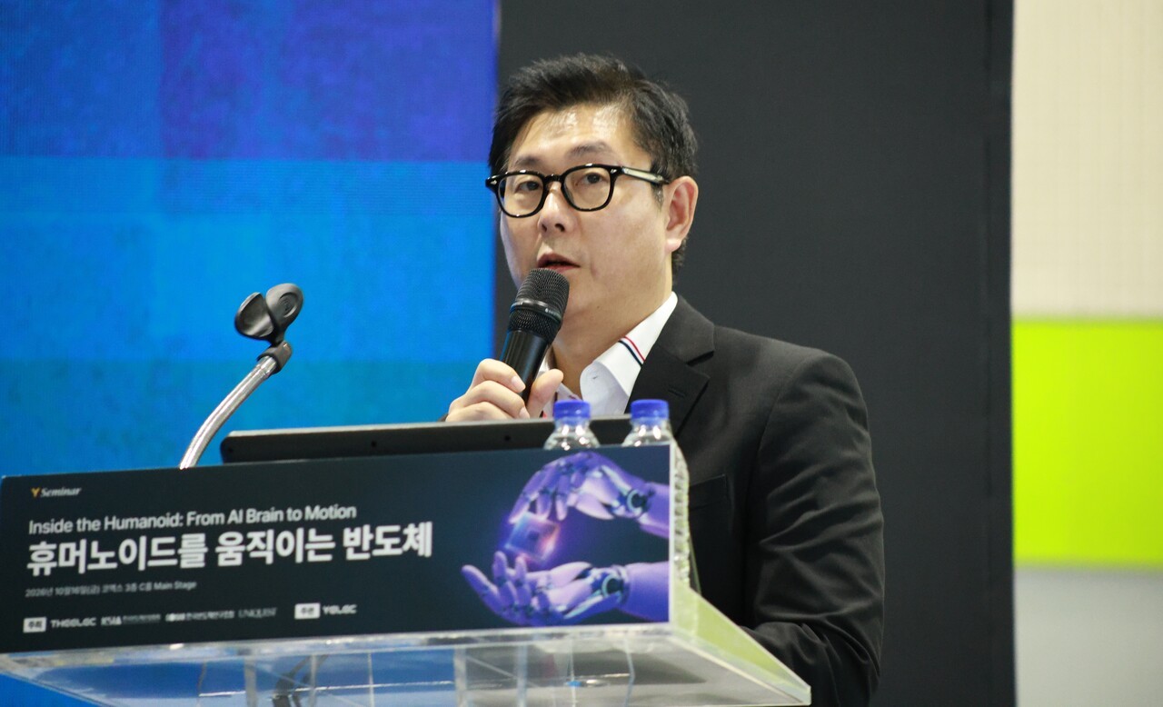 A speaker is presenting at the Inside the Humanoid: From AI Brain to Motion seminar, standing at a podium with a microphone and computer setup.