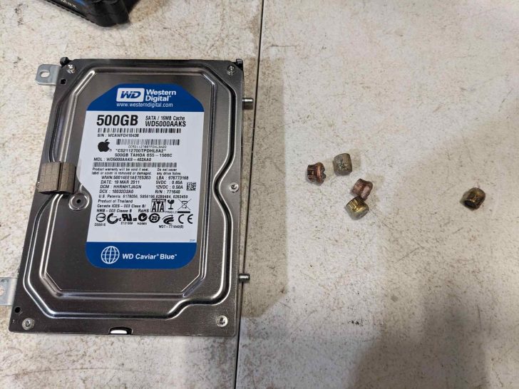 Un disque dur Western Digital Caviar Blue 500GB (modèle WD5000AAKS) posé sur une surface à côté de six petites capsules d'amorce utilisées.